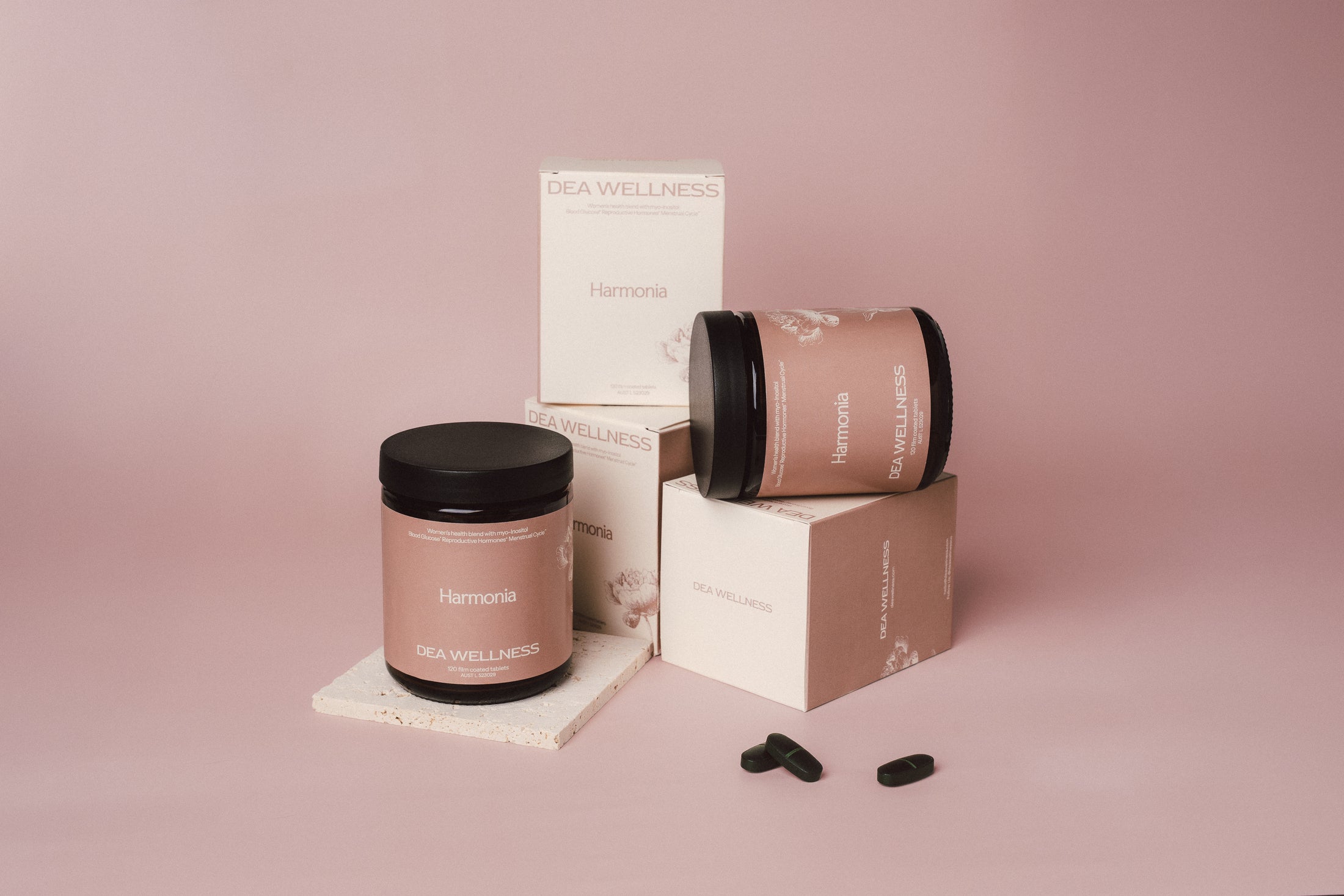 A jar and box set of DEA Wellness Harmonia capsules, styled on a dusty pink background with two capsules in the foreground.