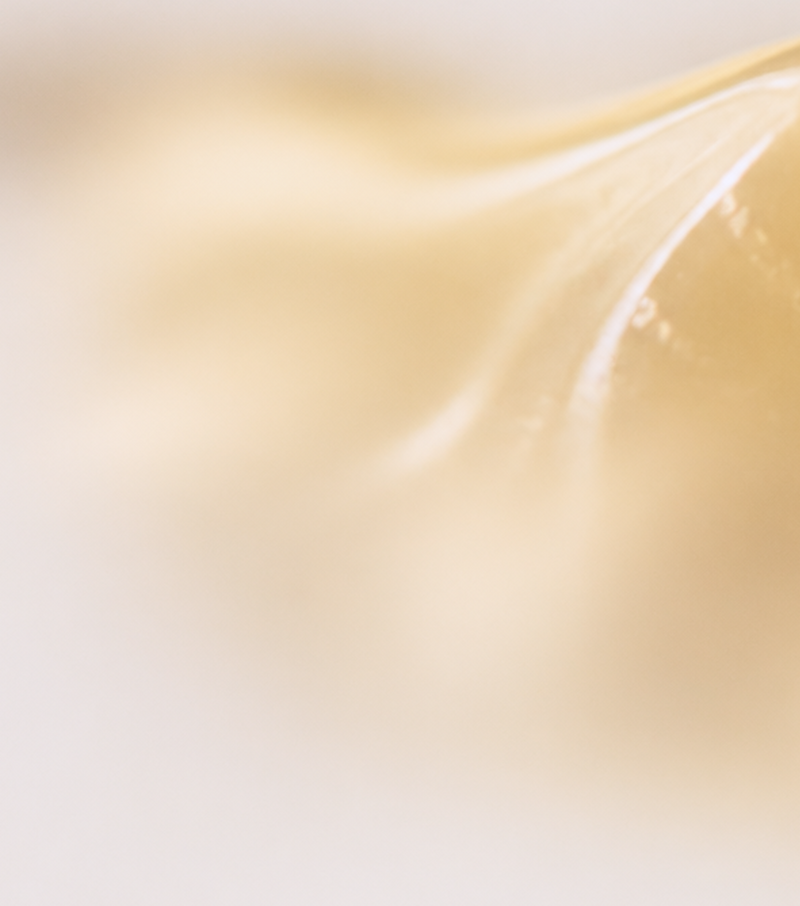 A close-up, abstract shot of a creamy, pale yellow cosmetic or food product with soft, flowing textures and a warm, glossy sheen.