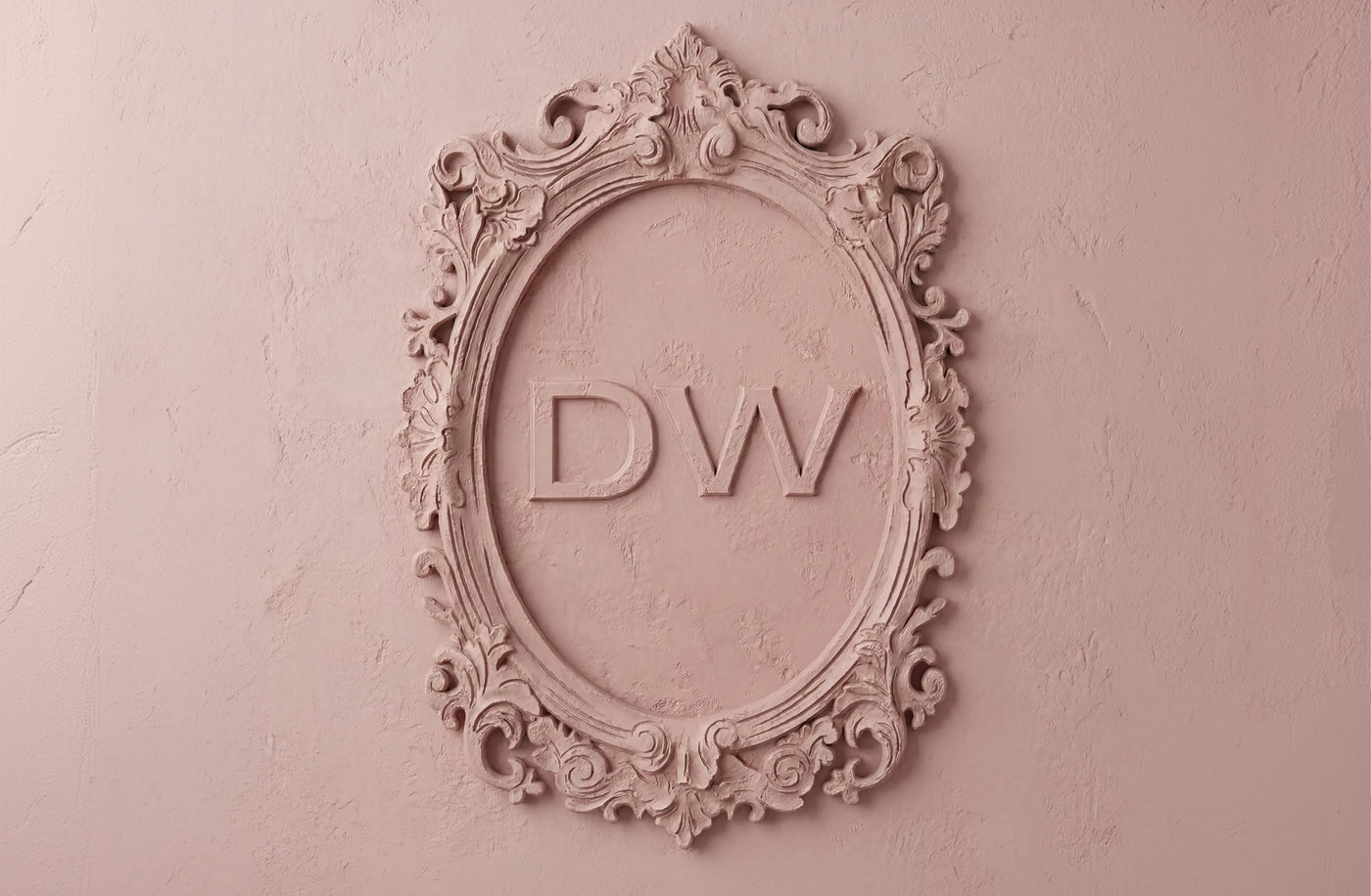 An ornate oval decorative frame mounted on a textured pink wall, featuring the initials 'DW' in raised lettering in the center.