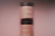 A close-up, vertically oriented shot of a Harmonia Sea Wellness bottle with a black cap and a warm beige-pink body, set against a matching soft pink background.