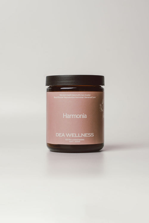 A dark amber glass jar with a matte black lid and a dusty pink label reading 'Harmonia' and 'DEA WELLNESS', centered on a light gray background.